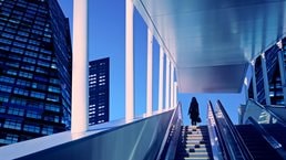 Early evening at modern business district with silhouette of businesswoman on top of a moving escalator.