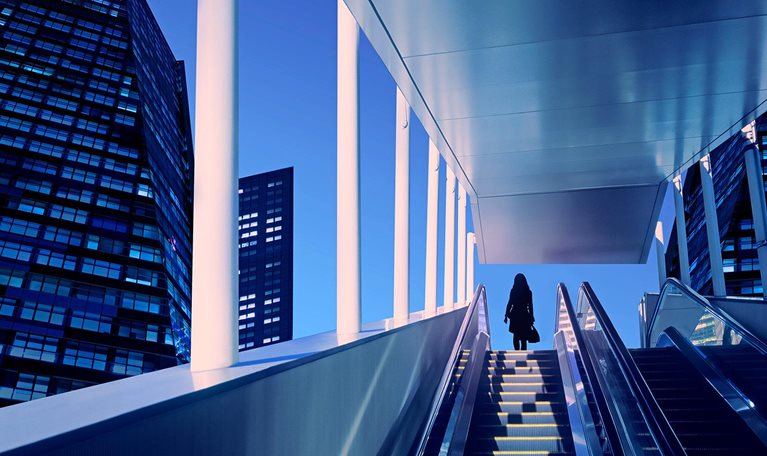 Early evening at modern business district with silhouette of businesswoman on top of a moving escalator.