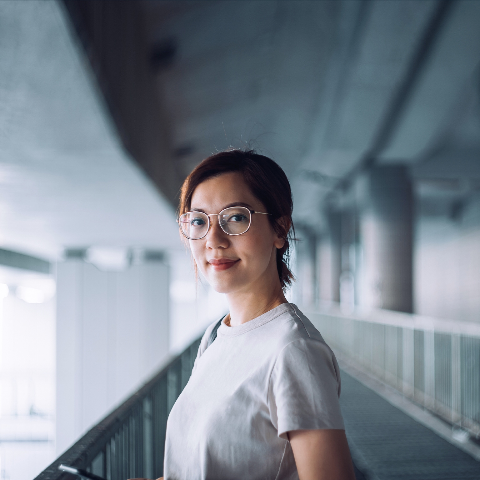 Portrait of confident and successful young Asian businesswoman looking at camera with smile, standing against urban bridge in the city - stock photo