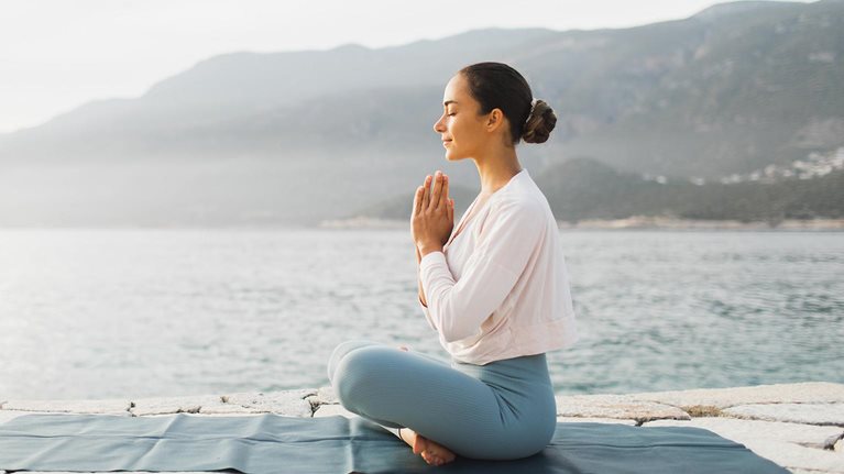 Young woman praying and meditating outdoors by seaside.