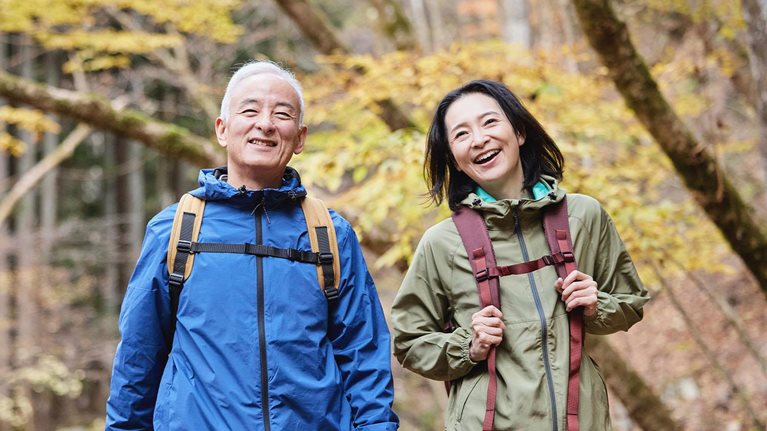 Smiling Japanese senior couple hiking in an autumn forest