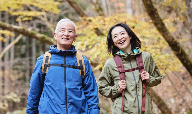 Smiling Japanese senior couple hiking in an autumn forest