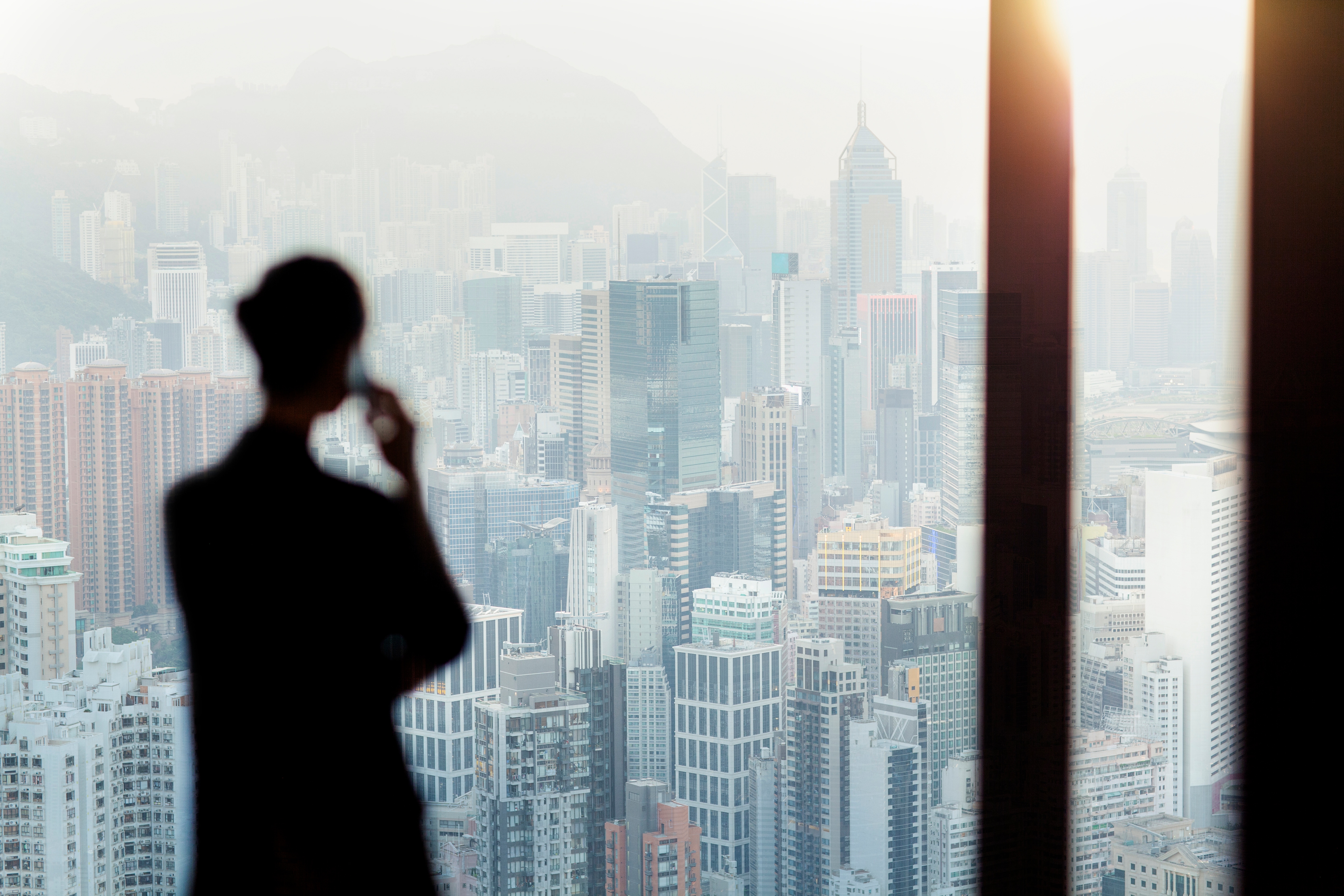 Silhouette of a woman with a phone i front of a glass widow facing a brightly lit skyline