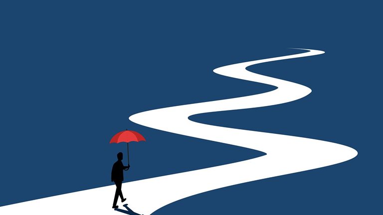 Businessman walks along a long, winding road holding an umbrella.