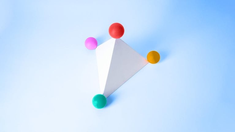 A white triangular pyramid with four balls of varying colors situated at each of the pyramid's points.