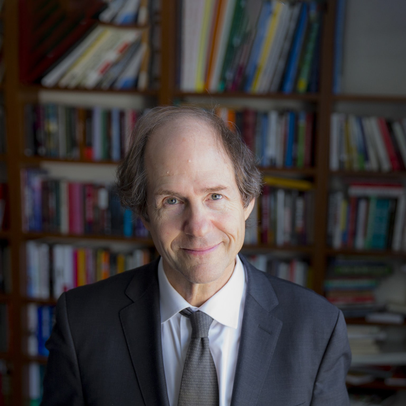 Portrait of Cass Sunstein in front densely filled bookcases.