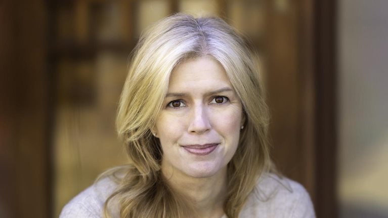 Gwendolyn Bounds is depicted in a portrait leaning forward with a light smile as she dons a soft beige cashmere sweater.