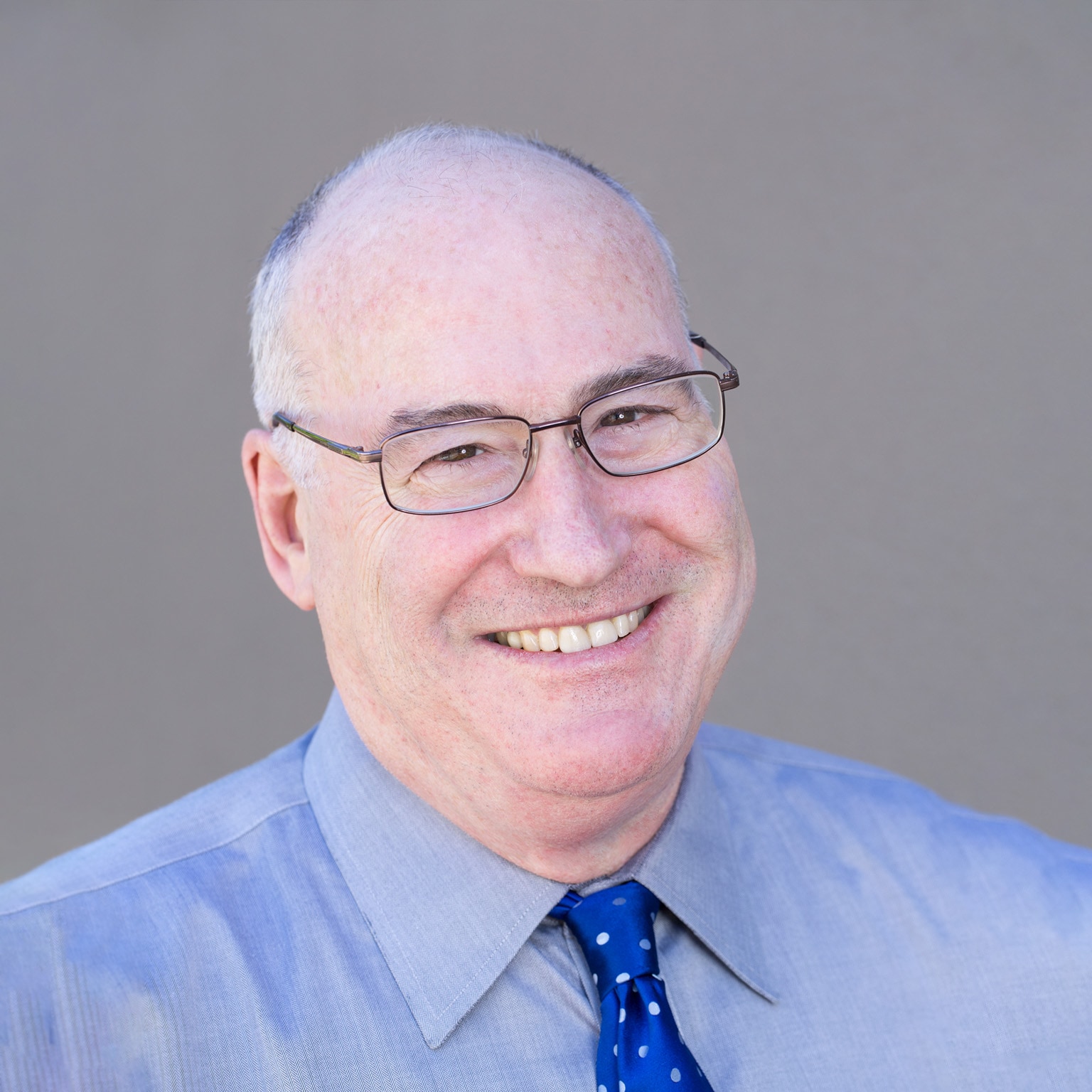 Portrait of a smiling Robert Sutton in a blue collared shirt and tie.