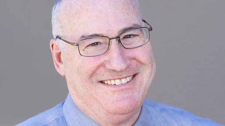 Portrait of a smiling Robert Sutton in a blue collared shirt and tie.