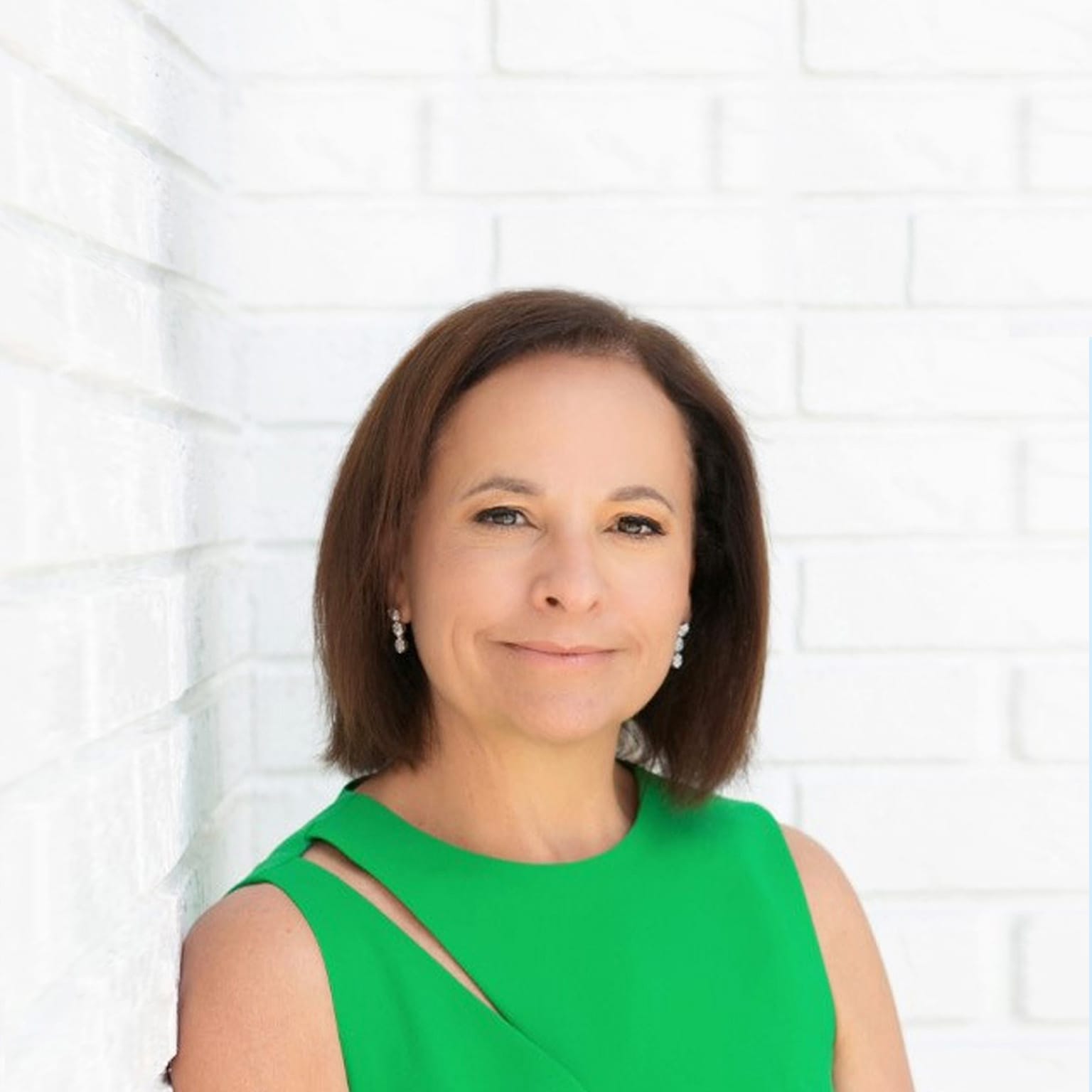 Portrait of Grace Puma with a confident smile and leaning on a white brick wall.