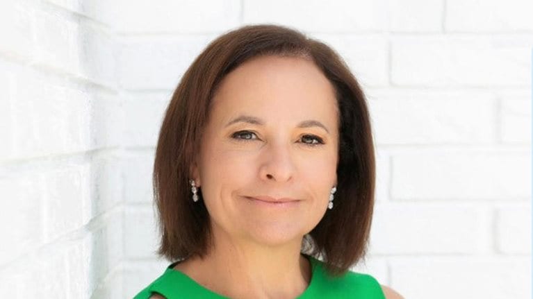 Portrait of Grace Puma with a confident smile and leaning on a white brick wall.