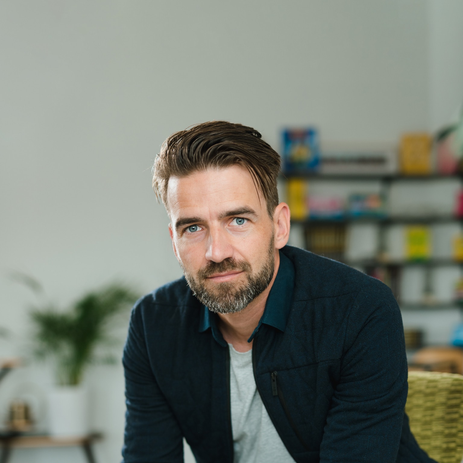 Mark Tuitert is depicted in a portrait wearing a navy blue overshirt with a collar, seated and leaning forward with evident interest. His hair is styled in a sleek side sweep and he sports a well-groomed beard.