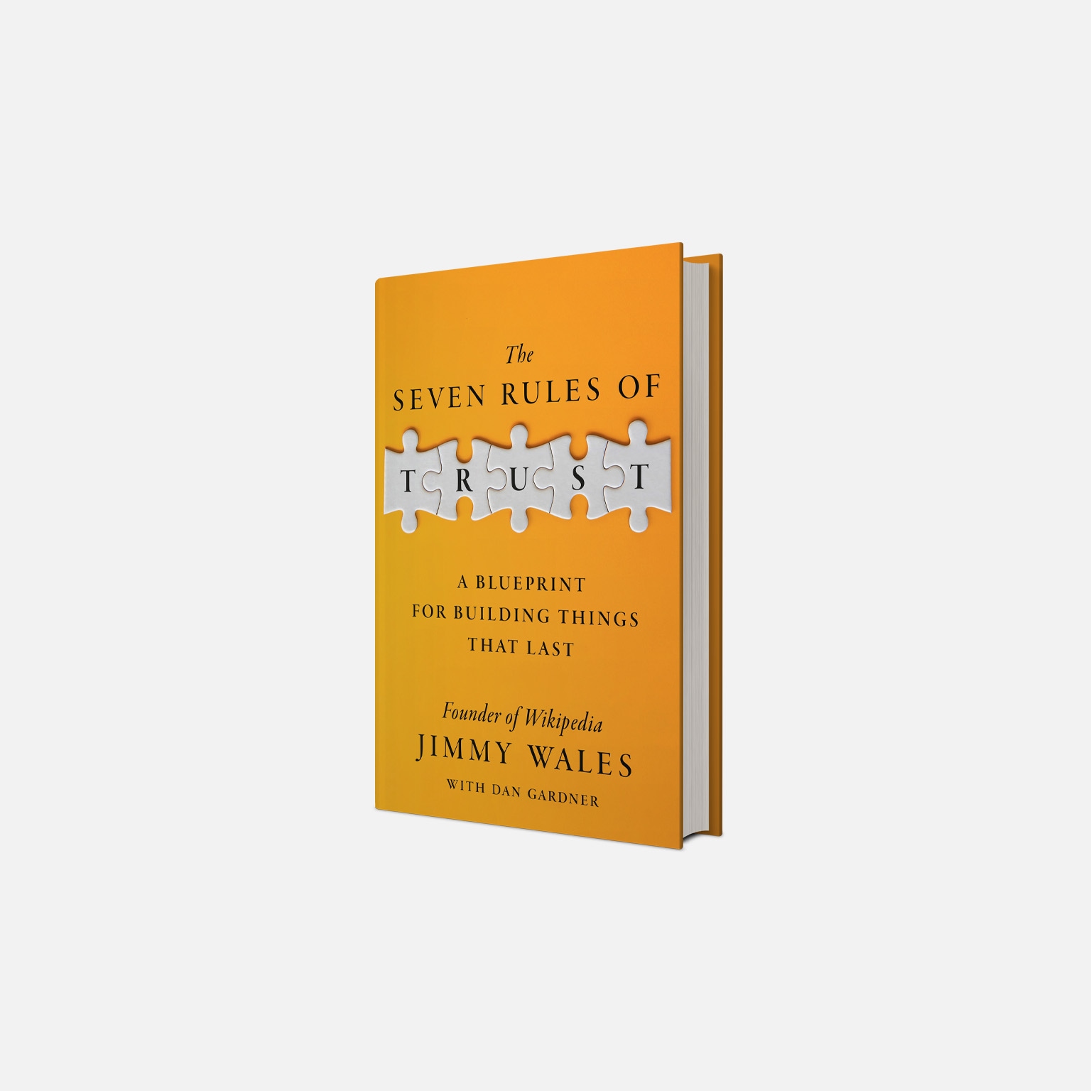 A book titled "The Seven Rules of Trust: A Blueprint for Building Things That Last" by Jimmy Wales. The word "TRUST" is spelled out in white letters on puzzle pieces that are on the orange cover of the book.