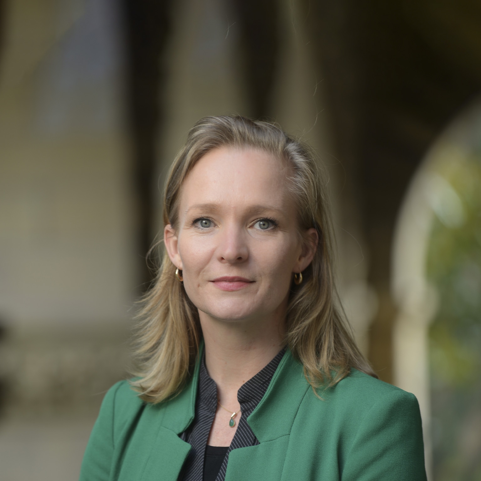 Marietje Schaake is depicted in a green blazer, with a subtle smile and a confident gaze.