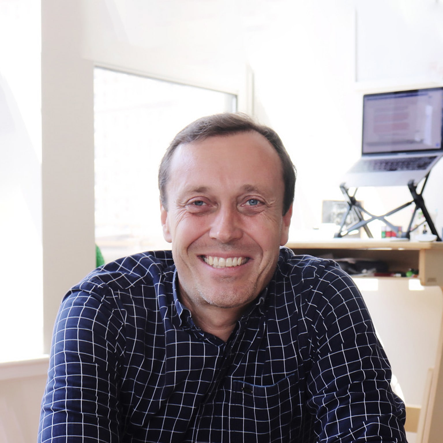 Stephan Meier sporting a navy blue checkered button-down shirt and a smile, while seated in a well-lit, private office.