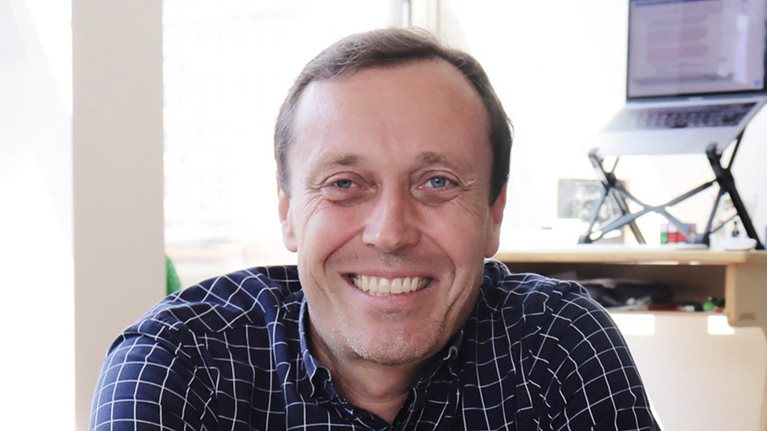 Stephan Meier sporting a navy blue checkered button-down shirt and a smile, while seated in a well-lit, private office.