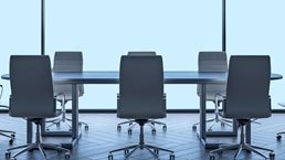 A modern boardroom table and chairs with large windowpanes behind it.