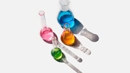 Laboratory glassware containing liquids of different colors on a light gray background.