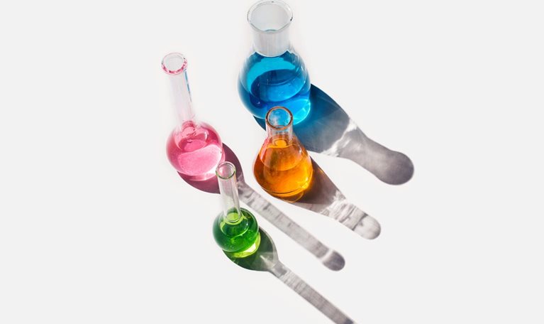 Laboratory glassware containing liquids of different colors on a light gray background.