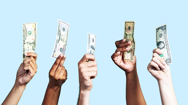 A diverse group of hands holding up US dollar banknotes of various denominations on light blue background.