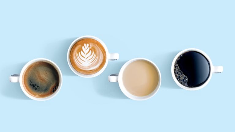  Overhead view of cups with different types of coffee. One of the cups sits higher up in the frame with a foam flourish on top.