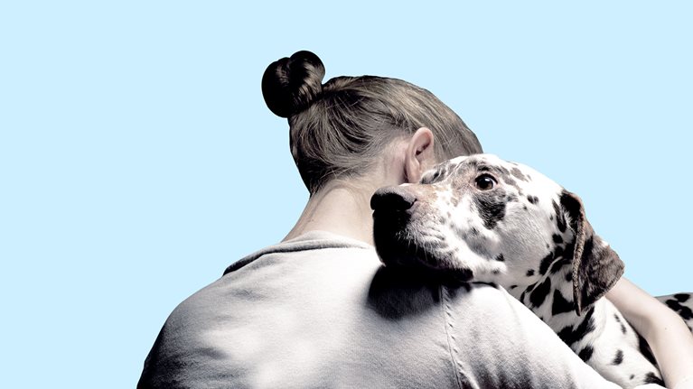 A close up of a woman embracing a Dalmatian. The woman is facing away from the camera with the endearing expression and kind eyes of the Dalmatian facing forward. 