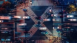 Overhead view of large roadway crosswalk section with heavy volume of cars passing in various directions.