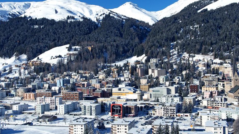 On a bright winter day, Davos, Switzerland can be seen from above, with a snowy landscape and the Schtzalp mountain in the distance.