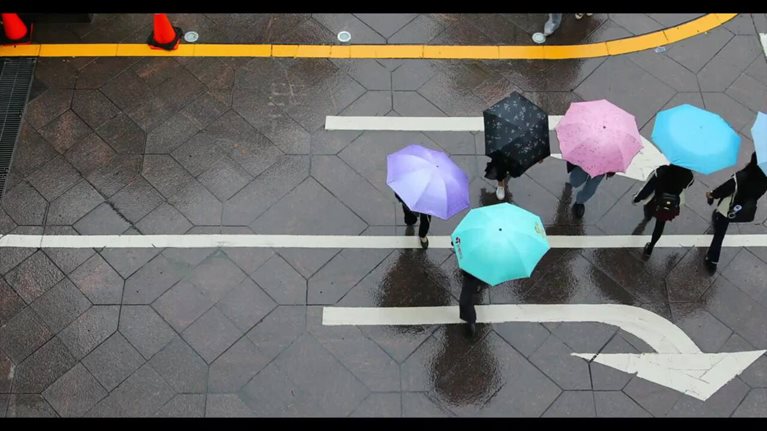 Overhead view of people walking with colorful umbrellas across a street intersection 