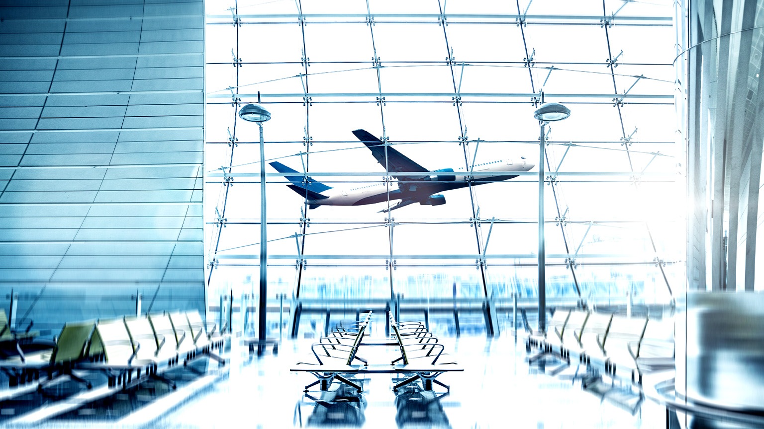 View from the inside of a modern bright airport with an airplane taking off outside the window.