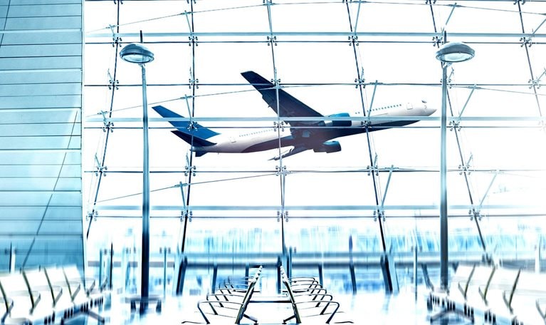 View from the inside of a modern bright airport with an airplane taking off outside the window.