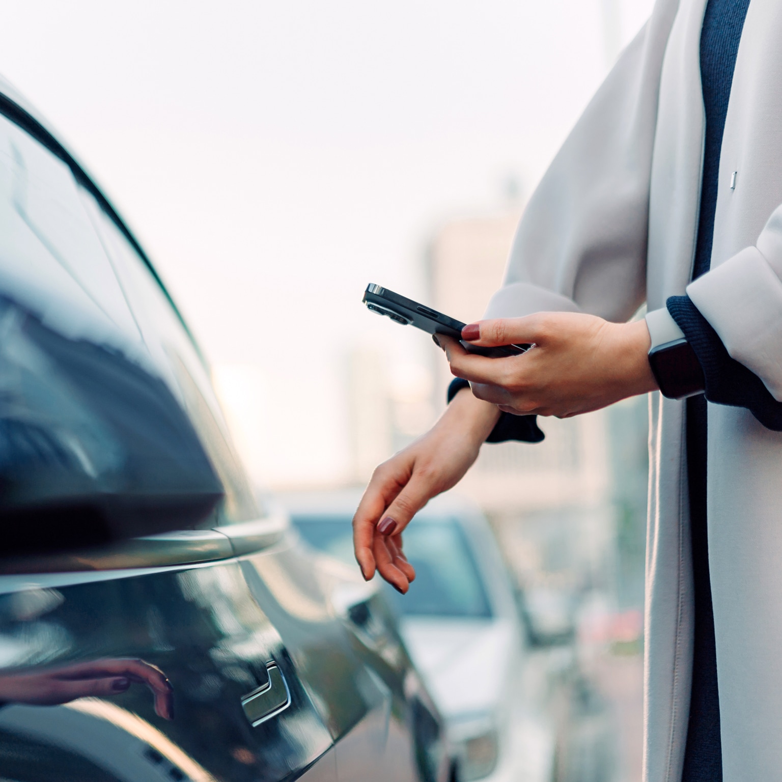 Close up of young Asian woman using mobile app device on smartphone to unlock the doors of her intelligence car in city street