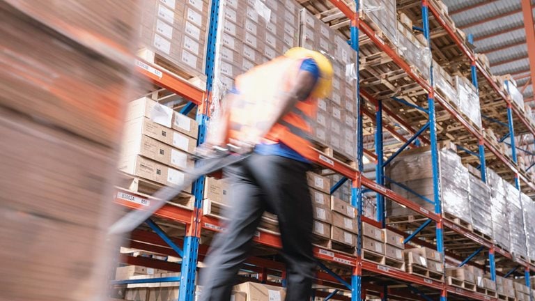 Motion blurred of warehouse worker moving boxes on pallet in warehouse
