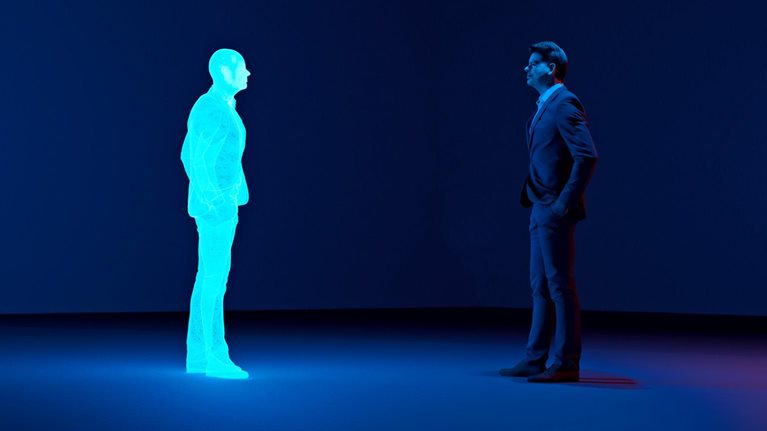 Man stands in a room looking at an avatar of himself. The clone is shown as a hologram.