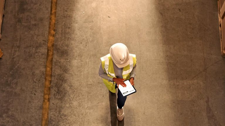 Worker wearing hard hat checks stock and inventory using digital tablet computer in a warehouse
