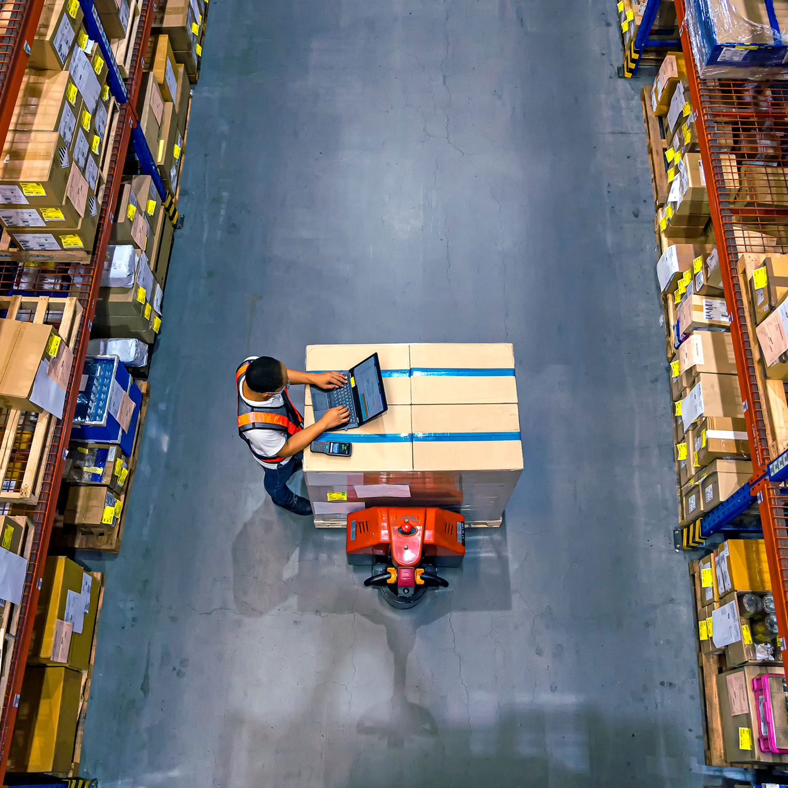 Top view of warehouse worker using laptop to check location of goods