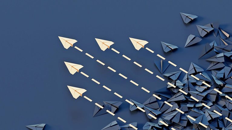 Conceptual image showing a jumble of dark paper planes with an organized group of colored planes flying through and above them.