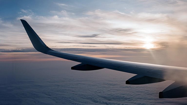 Wing of an airplane mid air, flying through the clouds at sunset