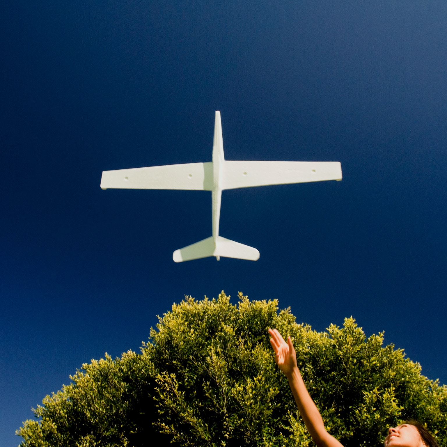 photo girl with outstretched arm as model plane flies above
