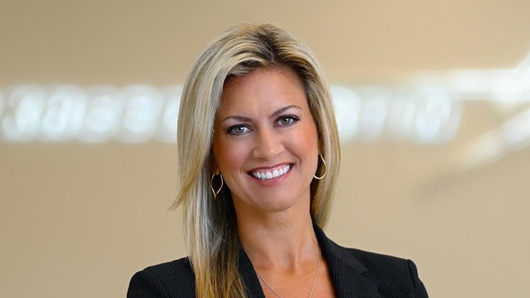 Portrait of Stacy Kubicek, who is wearing a sports jacket and exuding confidence. The Lockheed Martin logo is visible in the background, albeit slightly blurred.