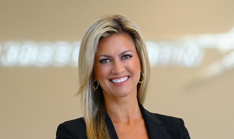 Portrait of Stacy Kubicek, who is wearing a sports jacket and exuding confidence. The Lockheed Martin logo is visible in the background, albeit slightly blurred.