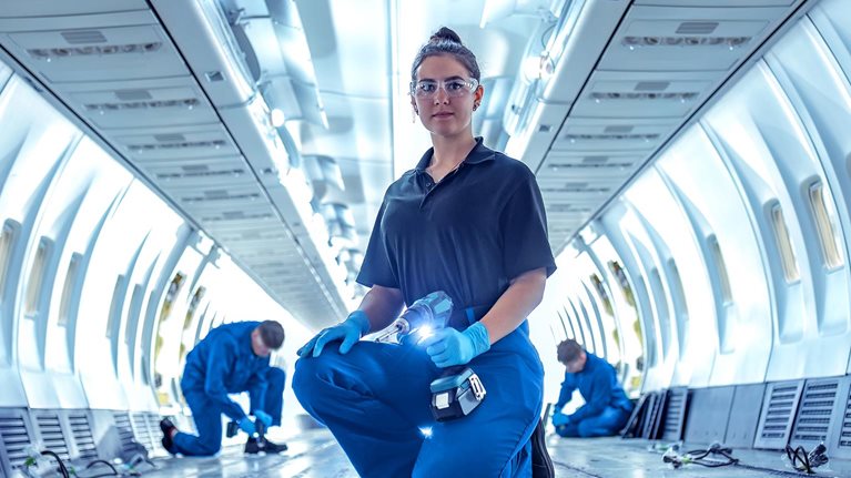 Portrait of female apprentice aircraft maintenance engineer in empty jet - stock photo