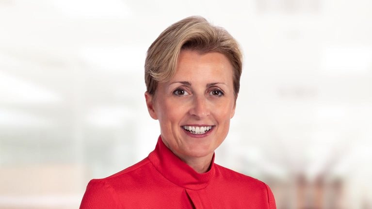 Portrait of a smiling Nikki Grady-Smith in a red high-neck blouse.