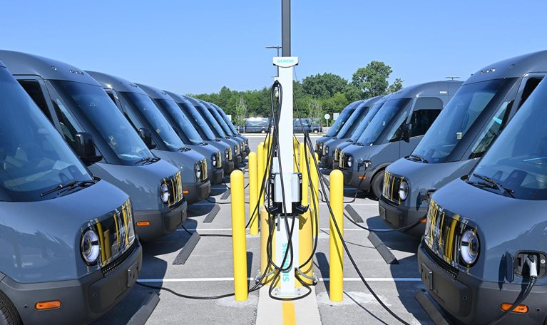 Rivian trucks, facing each other, plugged in and charging. - stock photo