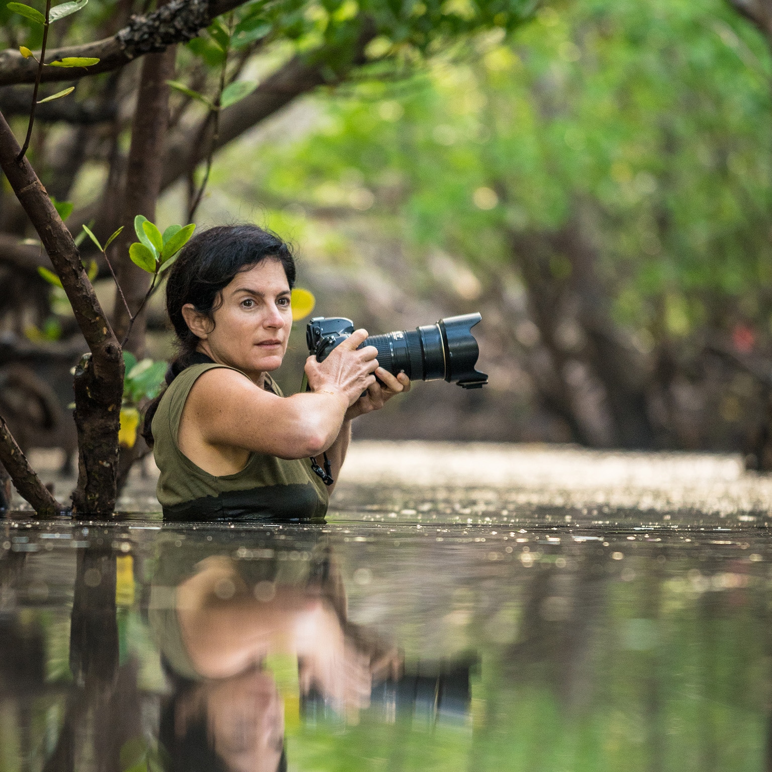 Ami Vitale, waist-deep in water, holds her camera, looking for the next shot. - photo