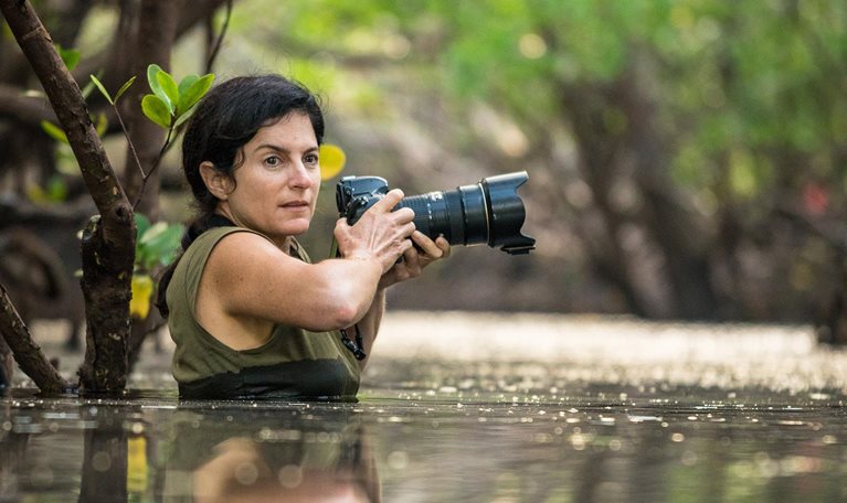 Ami Vitale, waist-deep in water, holds her camera, looking for the next shot. - photo
