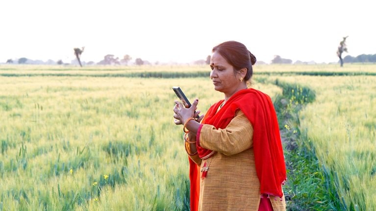 An Indian woman standing among agricultural fields looking into a mobile phone