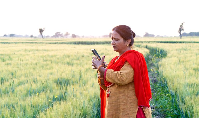 An Indian woman standing among agricultural fields looking into a mobile phone