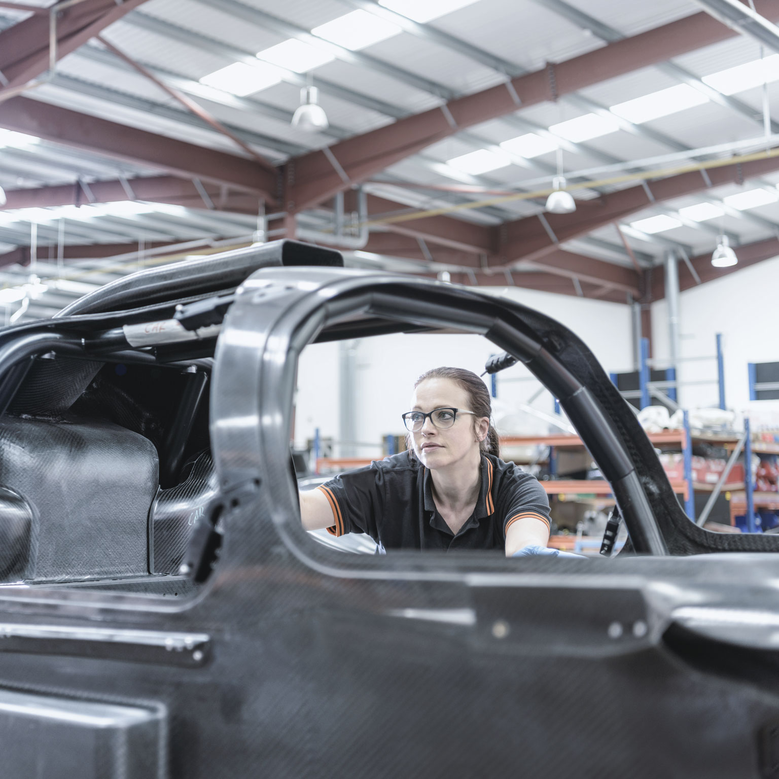 Female engineer inspecting carbon fiber body in racing car factory