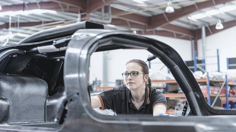 Female engineer inspecting carbon fiber body in racing car factory